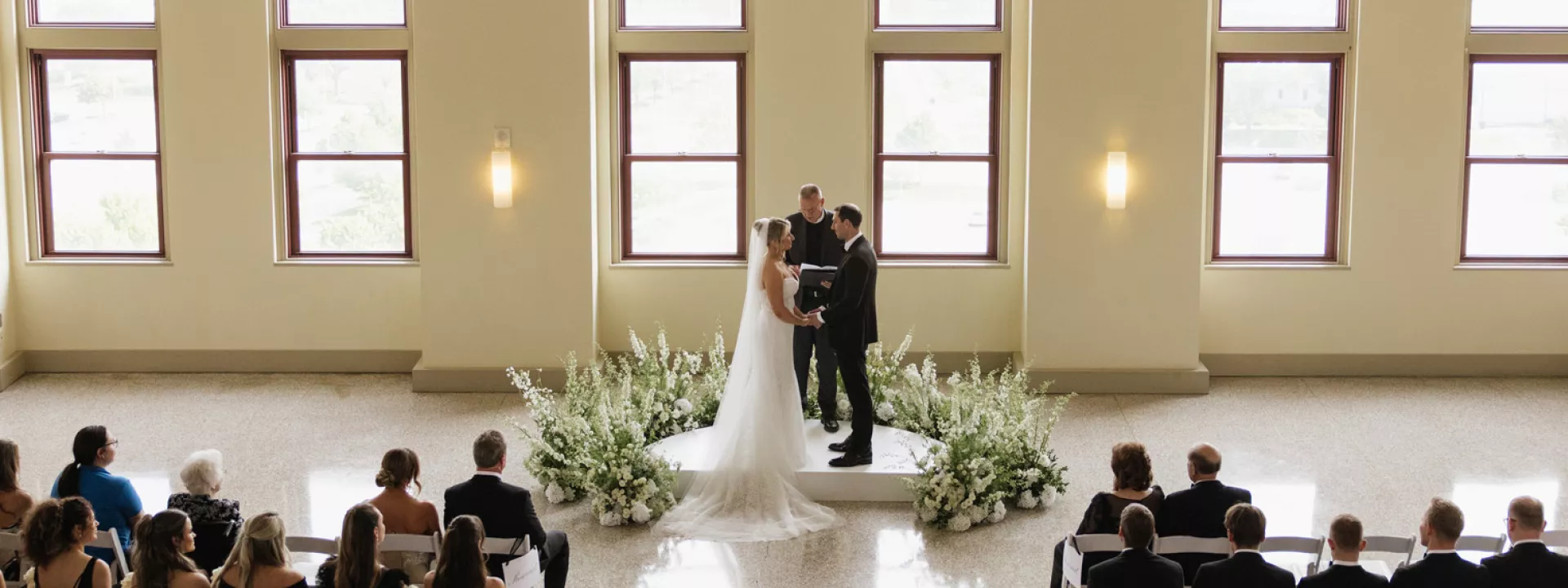 Bride and groom standing at the altar against a backdrop of floor-to-ceiling windows at Lumber Exchange Ballrooms
