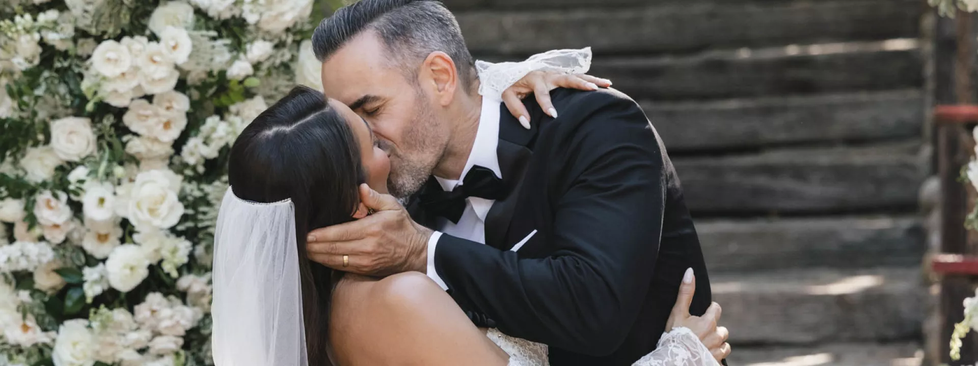 Bride and groom seal their vows with a kiss framed by an arch of lush white florals