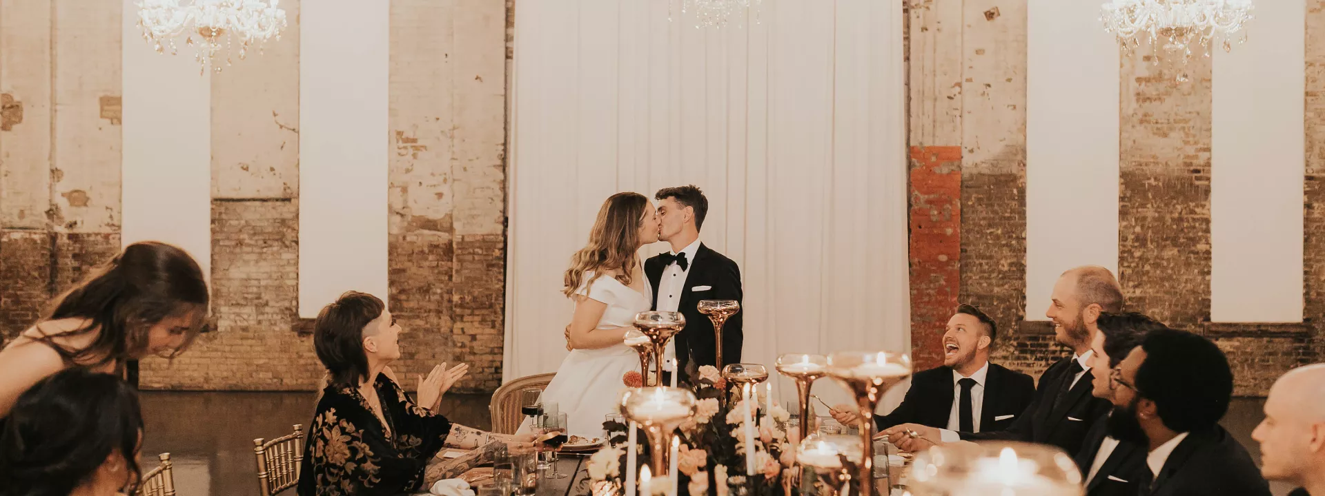 Madison and Robert Share a Kiss at the Head of their Table in Modern Industrial Wedding at Northern Pacific Center
