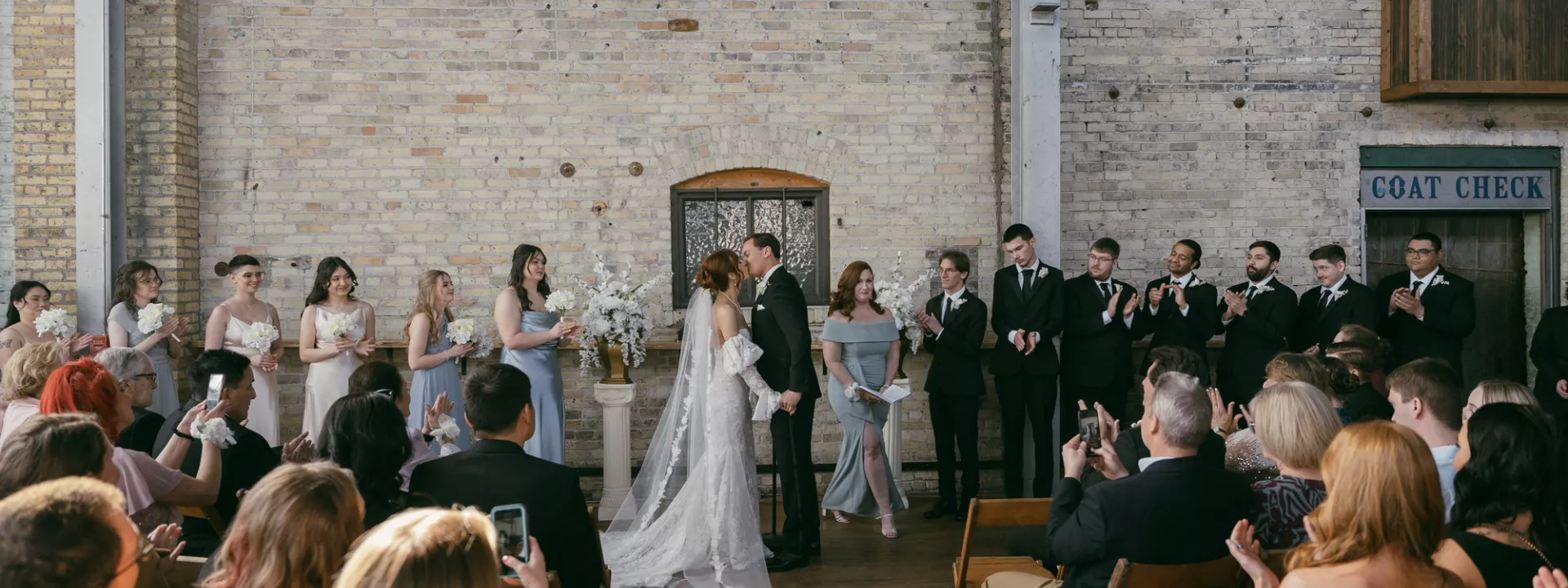 Bride and groom stand at the altar with bridal party framing them against the industrial interior of The Cooperage