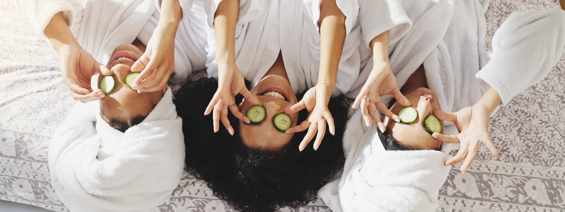 Bridesmaids in white robes relaxing during a wellness-focused bachelorette party with cucumber eye masks and spa treatments