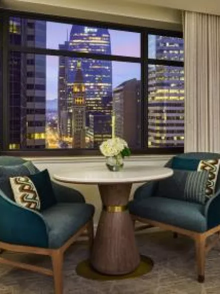 Cozy up in the stylish queen room sitting area at the Ritz-Carlton, Denver, showcasing plush teal chairs and a stunning cityscape view, perfect for a relaxing evening or intimate gathering