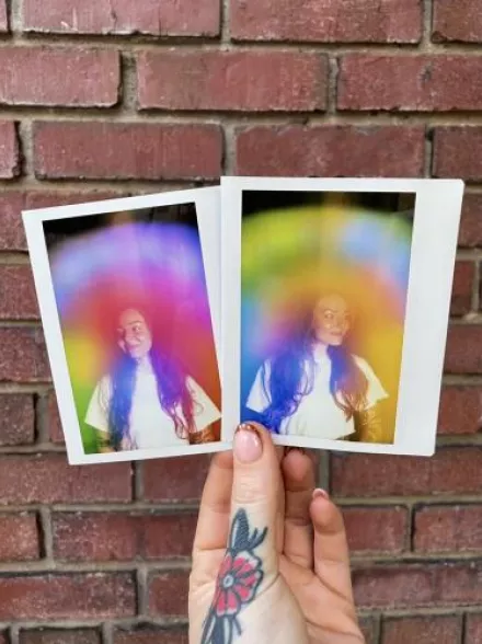 Two physical aura photograph polaroids by Vivid violet Aura side by side against a brick wall