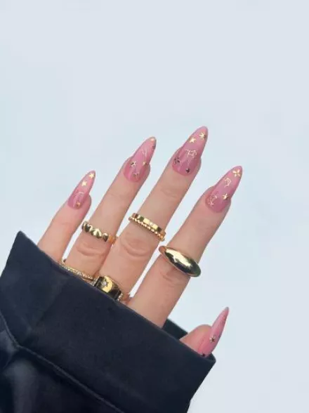 Hand peeking out of sweatshirt sleeve, with Deco Beauty nail sticker manicure and gold rings on fingers