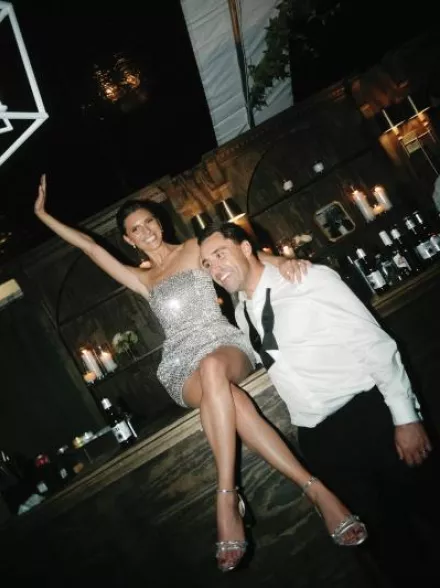 Bride poses on the bar in her sparkly after party attire with the groom by her side at Milwaukee Country Club