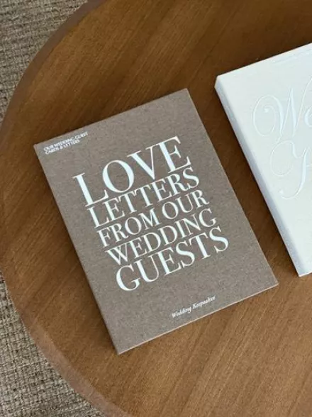 Brown linen keepsake box by The Ceremony Club with "Love Letters from our Wedding Guests" on cover, laying on wooden table