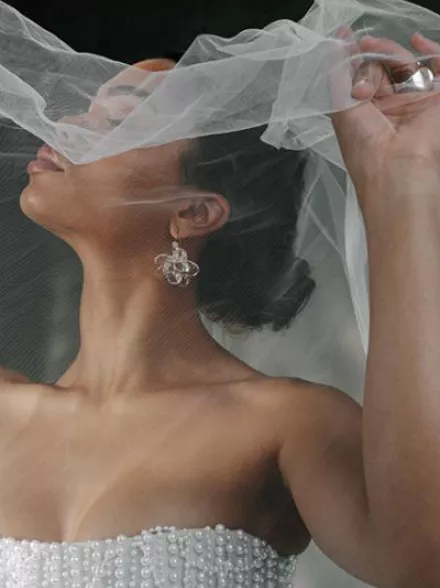 Model poses with holding veil over her face, showcasing stunning accessories in editorial shoot