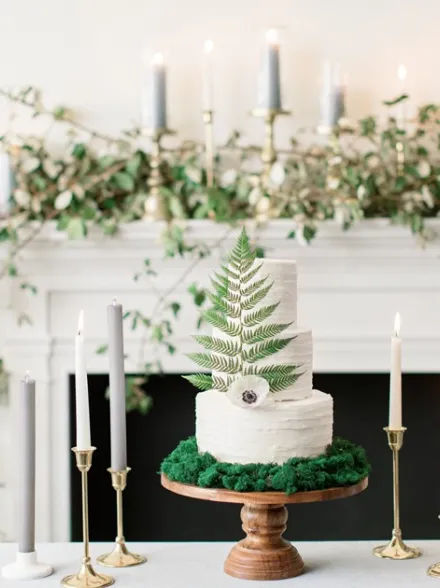 An understated delicacy by Cake Expressions, Inc. features textural icing and a pairing of a single fern and anemone to top it off. Presenting it atop an earthy bed of moss adds an organic vibe to its minimalist simplicity.