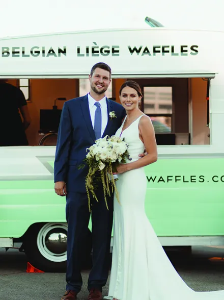 A couple stands in front of Belgian Liege Waffles, part of a new wedding trend: food stations.
